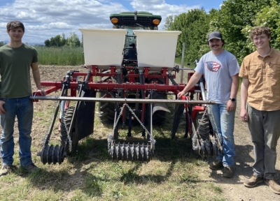 Michael Crain, Teagan Maloney, and Tyler Phelps stand in front of the interseeding technology they helped engineer. Fourth group member Spencer Von Flue is not pictured. (Tyler Phelps, Oregon State University)